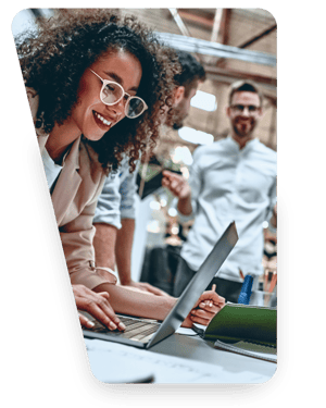 Smiling woman working on a laptop while two colleagues talk in the background of an open-plan office
